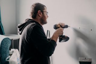 Adult man using a power drill indoors for home improvement in a well-lit room.